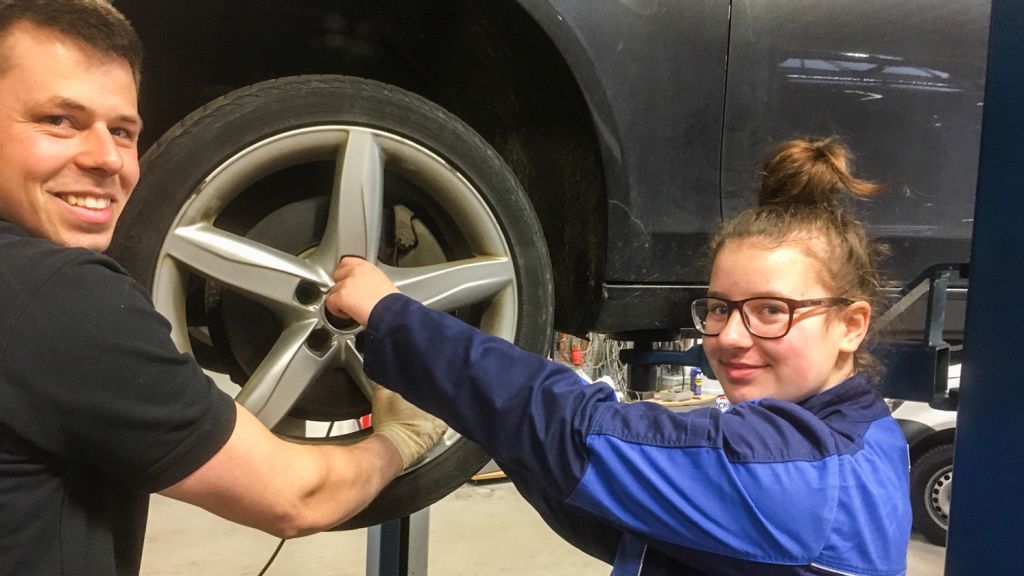 Kfz-Mechatroniker Felix Schröder hat Alicia Nowak zuschauen lassen, als er die Vorderachse eines Autos repariert hat. Bei der Montage der Räder reicht sie ihm die Muttern.