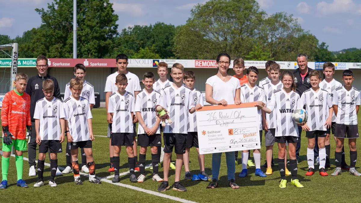 Kapitän Paul Bock und Sophie Feldmann überreichen den symbolischen Spendenscheck über 875 Euro an Rebecca Kranz vom Kinder- und Jugendhospiz Balthasar.