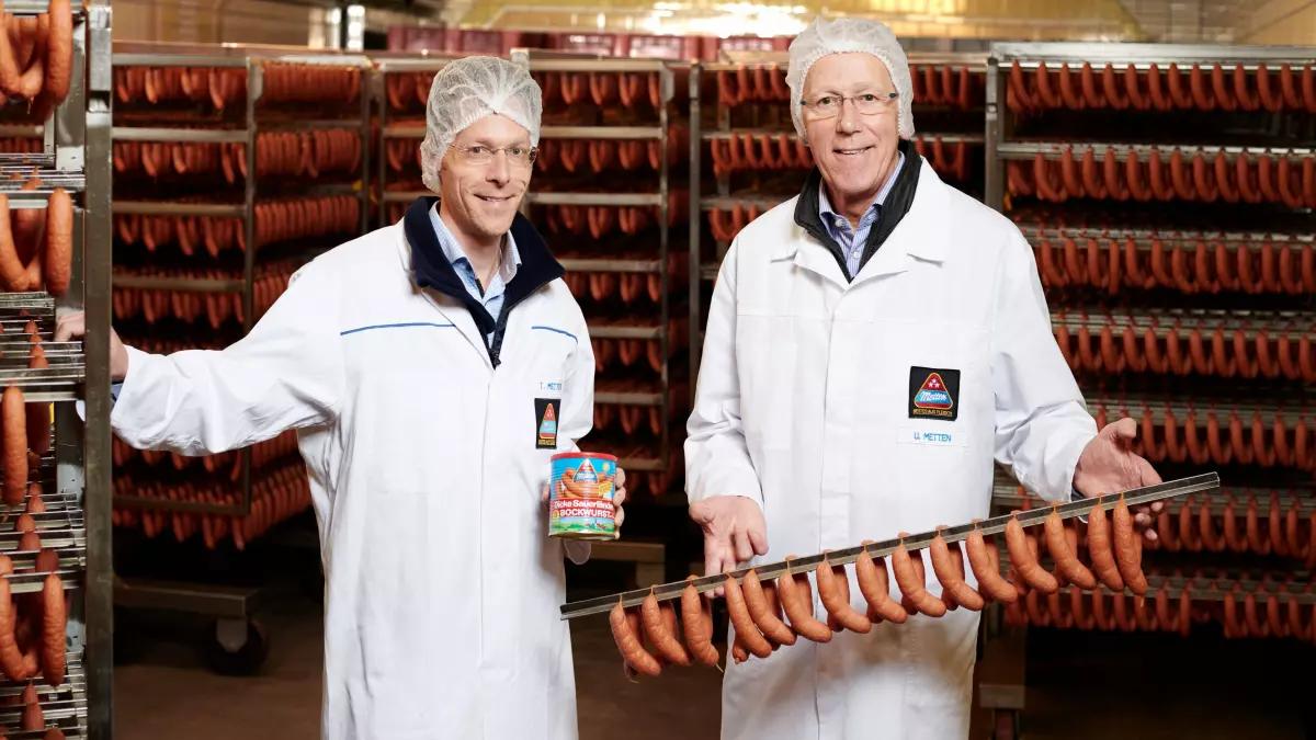 Die geschäftsführenden Gesellschafter Tobias und Ulrich Metten freuen sich über das Jubiläum der „Dicke Sauerländer“ Bockwurst.
