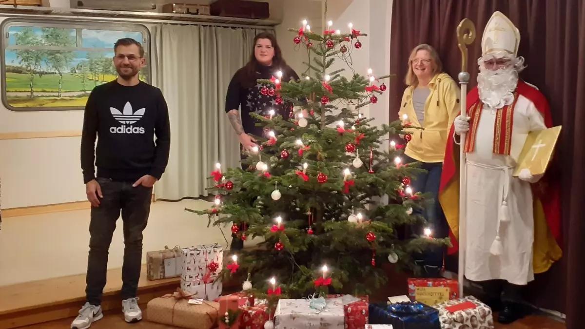 Marina Röhmann (2. v links) mit den Geschenken für die Kinder und einigen Unterstützern sowie dem Nikolaus am Weihnachtsbaum im Dorfsaal des Alten Bahnhofs in Hützemert.